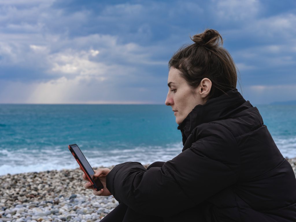 mulher olha celular sentada na praia da Península de Maraú